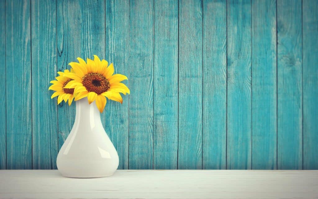 A vase of yellow flowers with a nice wooden backdrop painted blue.